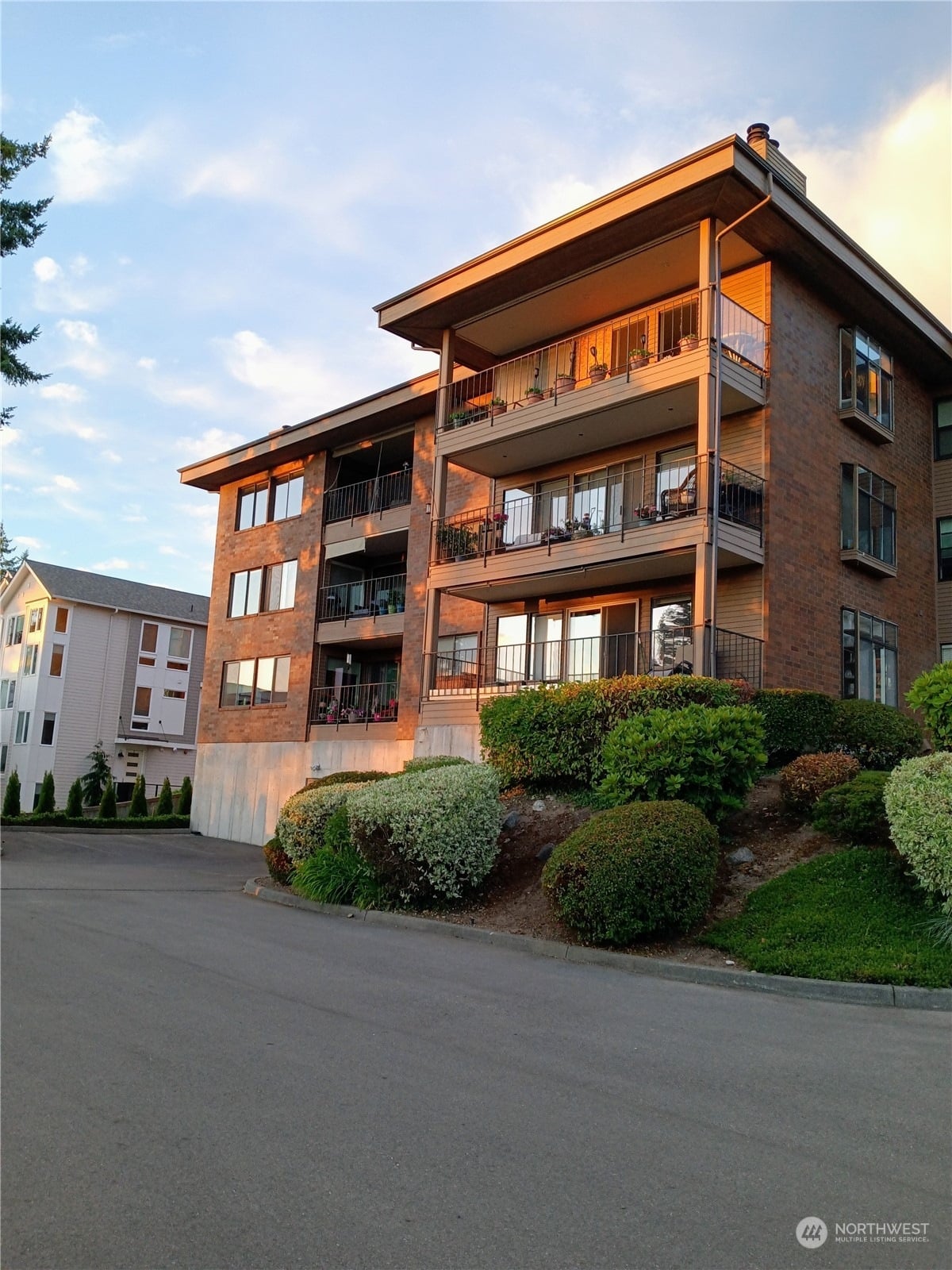 The Viewpoint Condominiums, a four-story brick building with wide balconies, above a landscaped berm in warm evening light