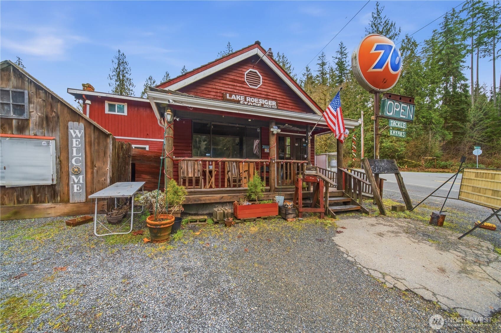 The red-sided Lake Roesiger Store with a covered wooden porch, a vintage 76 sign and tall firs behind